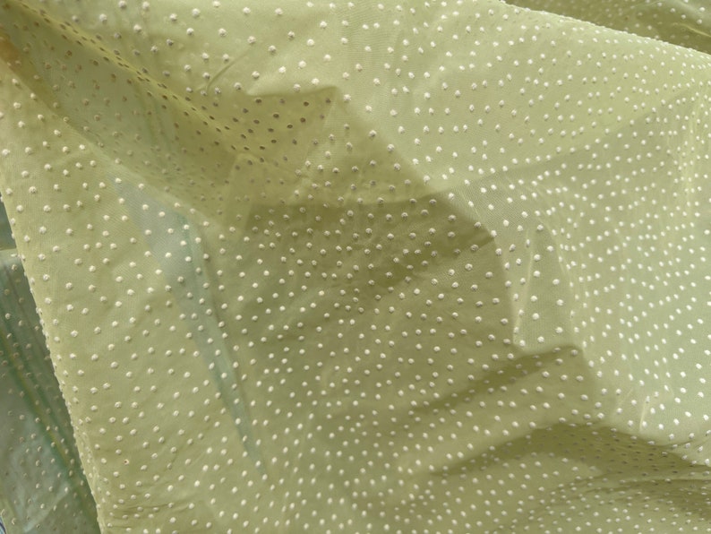 May include: A pale green fabric with a white polka dot pattern. The fabric is sheer and has a slightly textured surface.