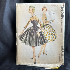 May include: Vintage McCall's sewing pattern for a misses and junior dress. The pattern is for a dress with a full skirt and a fitted bodice. The pattern is printed on a white background with black text. The pattern number is 5020. The bust size is 32.5 inches.