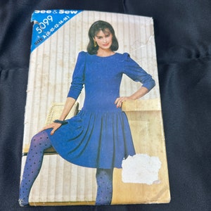 May include: A vintage sewing pattern envelope featuring a woman wearing a blue dress with a gathered skirt. The pattern number is 5099 and the size is A (8-10-12-14-16).