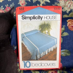 May include: A rectangular Simplicity House pattern envelope labeled 122 with the text 10 bedcovers. The front features a photograph of a light blue quilted bedspread with white trim and a white ruffled bed skirt on a bed with a headboard.
