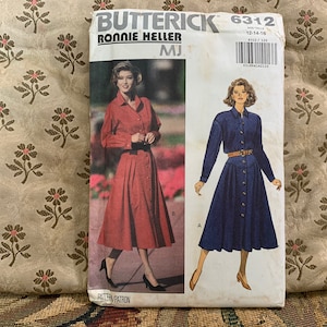 May include: A vintage Butterick sewing pattern featuring two dress designs. The pattern cover shows a red dress and a blue dress, both with button-down fronts and belted waists. The pattern number is 6312, and the size range is 12-14-16.
