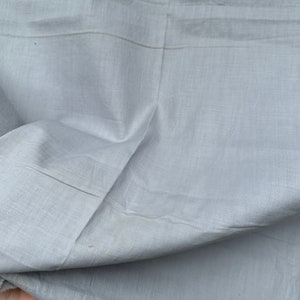 May include: A close-up of a light gray fabric with a smooth texture. The fabric is folded and has a slight sheen.