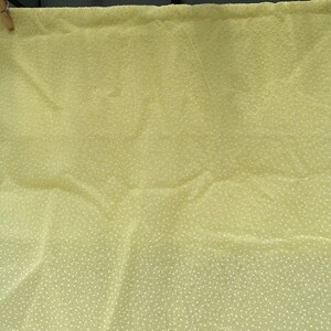 May include: A pale yellow fabric with a white polka dot pattern. The fabric is hanging on a clothesline.