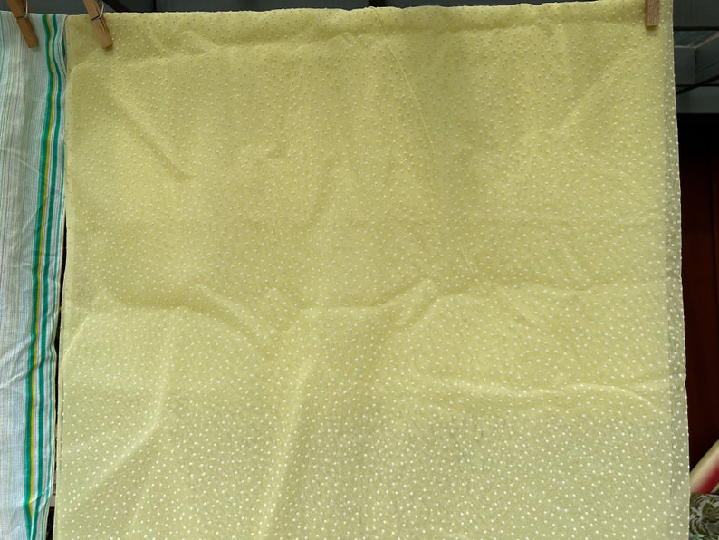 May include: A pale yellow fabric with a white polka dot pattern. The fabric is hanging on a clothesline.