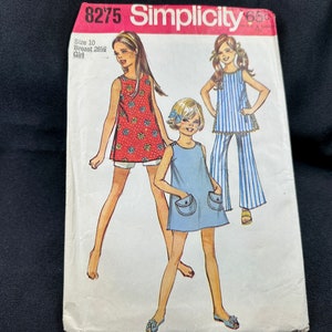 May include: Vintage Simplicity sewing pattern featuring illustrations of girls' clothing. The pattern includes designs for a red floral top, blue dress with pockets, and striped top with matching pants. The pattern is labeled size 10, breast 28.5 inches.
