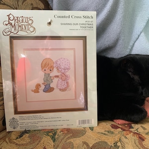 Op de afbeelding: Geteld kruissteekpatroon van Precious Moments met twee kinderen die een kerstcadeau delen met een puppy. Het patroon is getiteld "Sharing Our Christmas Together" en is genummerd #131-57.
