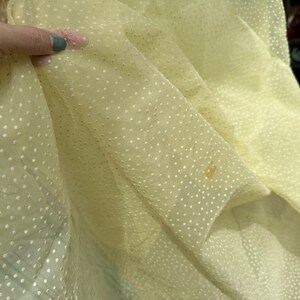 May include: Pale yellow sheer fabric with a white polka dot pattern. The fabric is slightly wrinkled and has a few brown stains.