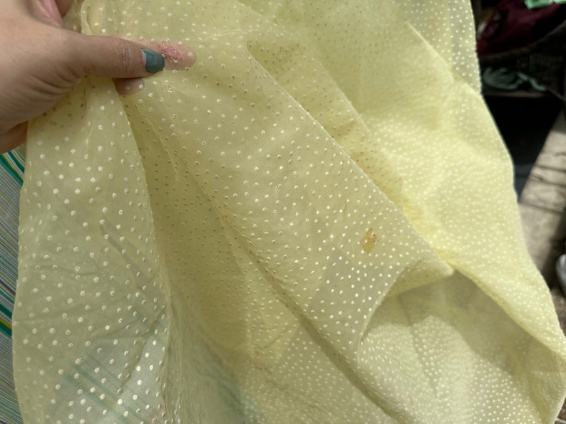 May include: Pale yellow sheer fabric with a white polka dot pattern. The fabric is slightly wrinkled and has a few brown stains.