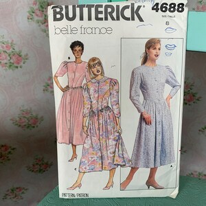 Könnte beinhalten: Ein Vintage-Butterick-Schnittmuster, Belle France 4688, mit Illustrationen von drei verschiedenen Kleiderdesigns. Der Schnittmusterumschlag ist weiß mit schwarzem Text und Bildern der Kleider in rosa, floralen und blauen Stoffen. Größe 8.