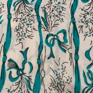 May include: White fabric with a repeating pattern of teal blue bows and black floral sprigs.