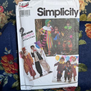 May include: A Simplicity sewing pattern envelope, number 7428, for the 2 Hour Express collection. The white paper packaging features illustrations of children wearing various colorful clown and jester costumes, including patterned jumpsuits.
