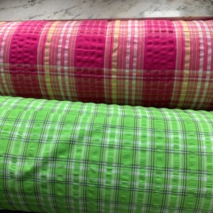 May include: Two rolls of fabric with a checkered pattern. The top roll is pink and white, and the bottom roll is green and white.
