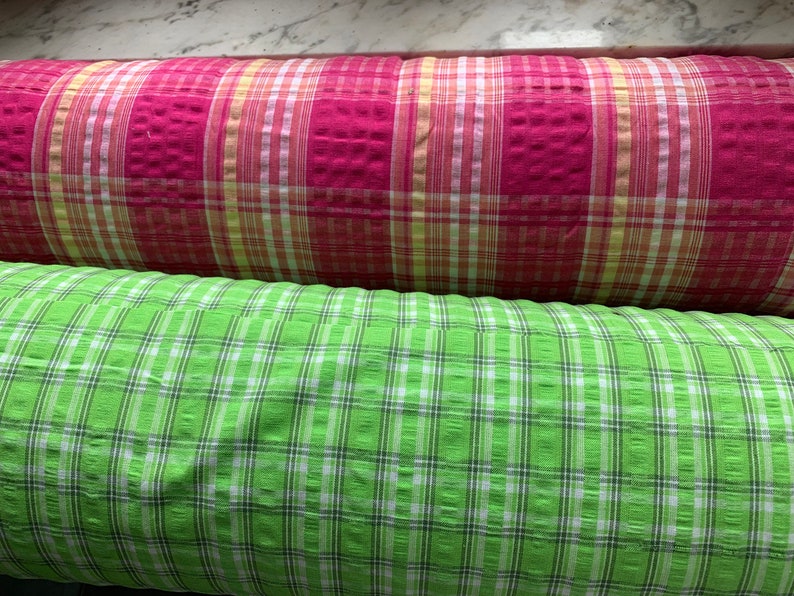May include: Two rolls of fabric with a checkered pattern. The top roll is pink and white, and the bottom roll is green and white.