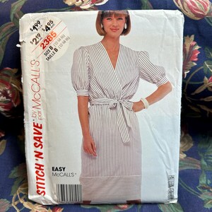 May include: A McCall's sewing pattern envelope featuring a woman in a striped wrap dress with a tie waist and short, puffed sleeves. The envelope includes the text "STITCH 'N SAVE" and "EASY". The size is indicated as B (12-14-16).