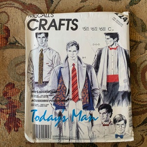 May include: A vintage McCall's Crafts sewing pattern for men's accessories. The pattern includes instructions for making a scarf, tie, and pocket square. The pattern cover features illustrations of men wearing the accessories.