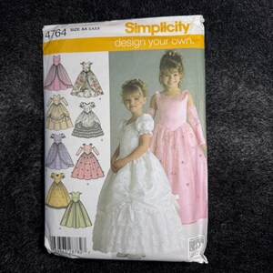 May include: Simplicity sewing pattern for girls' dresses. The pattern features illustrations of various dress designs, including a white dress with a bow and a pink dress with floral accents. The package also shows two young girls wearing the dresses.