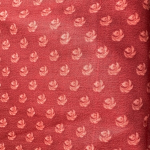 May include: Red fabric with a repeating pattern of small, light pink floral designs.
