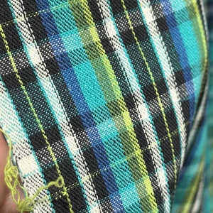 Puede incluir: Primer plano de una tela de cuadros azul, verde, negro y blanco con un patrón diagonal. La tela tiene una textura rugosa y está doblada.