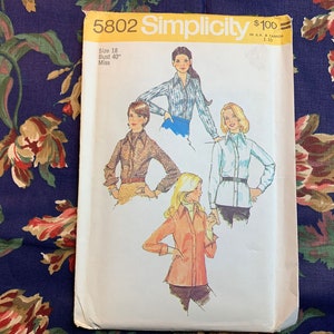 Pode incluir: Padrão de costura vintage Simplicity número 5802 para uma blusa feminina. O padrão é para o tamanho 18, busto 101,6 cm, e é para senhoritas. O padrão mostra quatro estilos diferentes de blusas, todas com mangas compridas e golas.