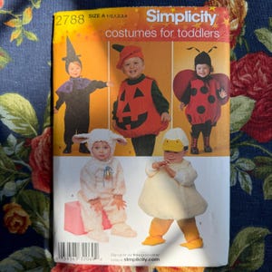 May include: Simplicity pattern 2788 for toddler costumes. The pattern features images of children dressed as a witch, pumpkin, ladybug, lamb, and duck. The pattern size is A 1/2, 1, 2, 3, and 4. The pattern is on a floral background.