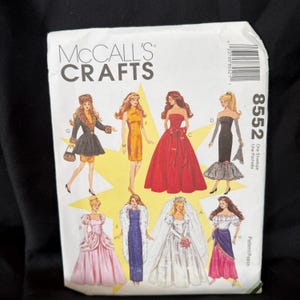 Peut inclure: Une enveloppe de patron de couture McCall's Crafts avec des illustrations de diverses robes et robes de soirée. L'enveloppe porte le numéro 8552 et les mots "One Envelope" et "Pattern/Patron". Le fond est noir.