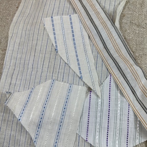 May include: A collection of fabric swatches with different striped patterns. The swatches are in various shades of white, blue, and purple.