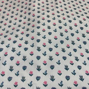 May include: White fabric with a repeating pattern of small pink and blue flowers with green stems. The fabric has a subtle texture.