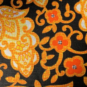 Könnte beinhalten: Ein schwarzer Stoff mit einem sich wiederholenden Muster aus orangefarbenen und gelben Blumen und Wirbeln. Der Stoff hat eine strukturierte Oberfläche.