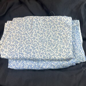 May include: Two pieces of white fabric with a blue floral pattern. The fabric is folded in half and the edges are visible.