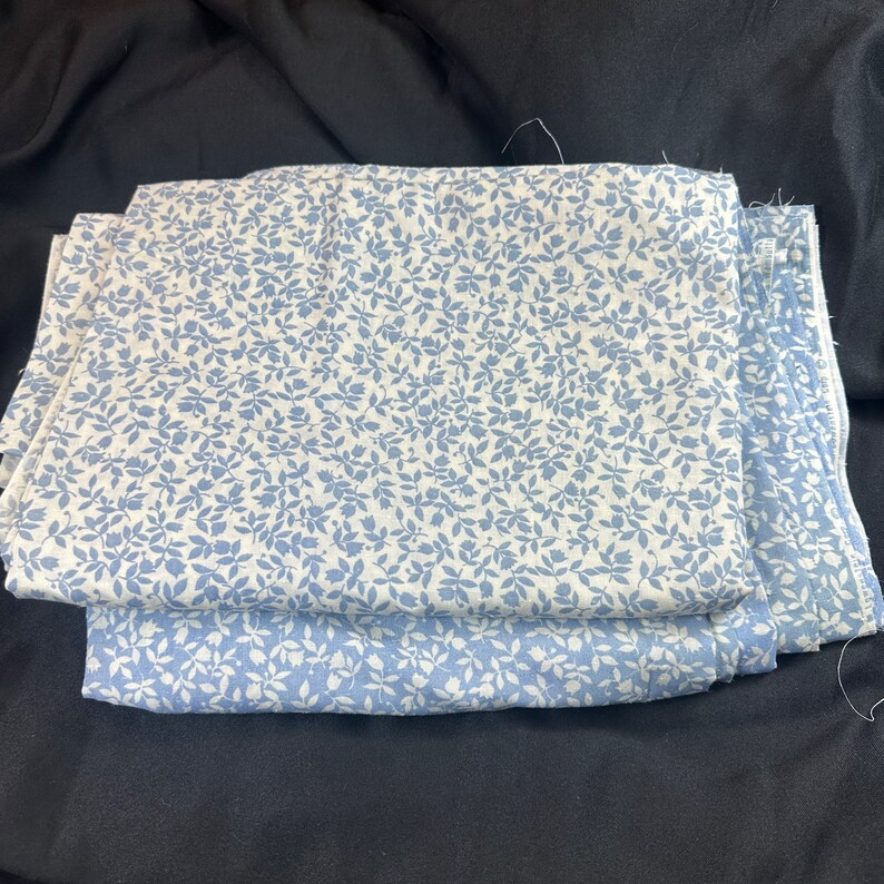 May include: Two pieces of white fabric with a blue floral pattern. The fabric is folded in half and the edges are visible.