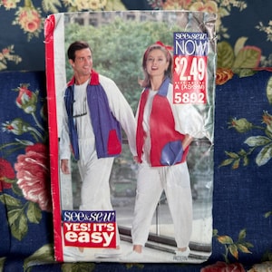 May include: A See & Sew sewing pattern envelope 5892 featuring two individuals wearing white long-sleeved shirts and pants with color-blocked vests. The left vest is purple with a red pocket, and the right vest is red with a purple pocket. Text includes See & Sew NOW 2.49 A (XS-S-M) 5892 and YES! IT'S EASY.