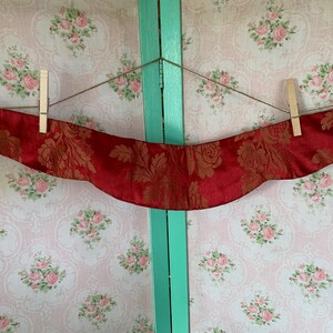 Peut inclure: Un collier en tissu rouge avec un motif floral doré, suspendu à une ficelle avec des pinces à linge.
