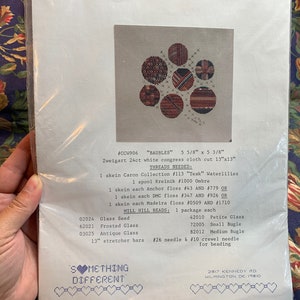 May include: A cross stitch pattern for a project called "Baubles" with a colourful geometric design. The pattern is 5 5/8 inches by 5 3/8 inches and requires Zweigart 24ct white congress cloth cut to 13 inches by 13 inches. The pattern also includes a list of threads and beads needed for the project.