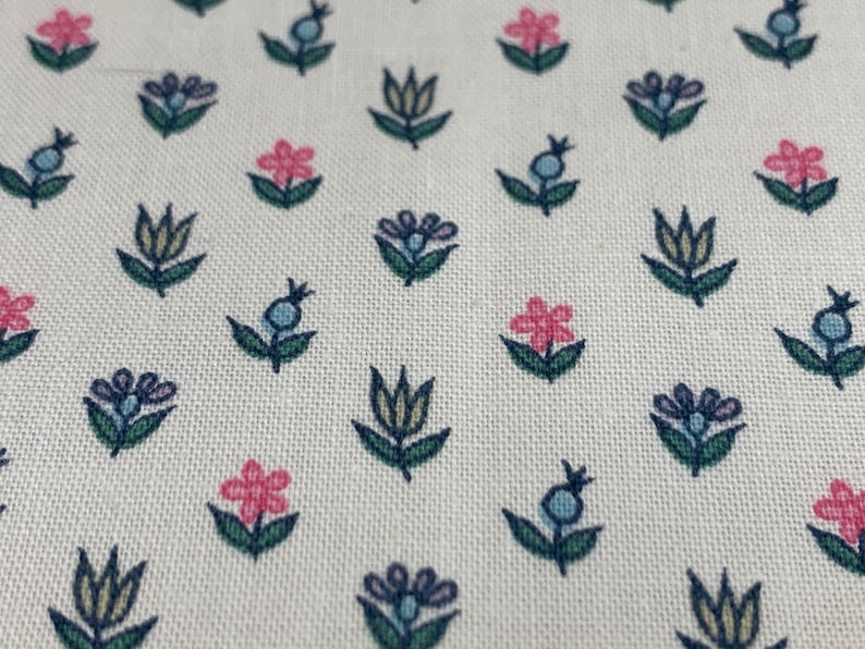 May include: White fabric with a repeating pattern of small blue, pink, and yellow flowers. The flowers are stylized and have a simple design.