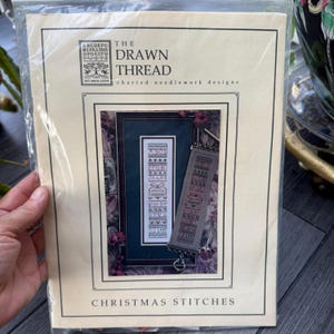 May include: A package for "The Drawn Thread" charted needlework designs. The package features a framed needlework design with the text "Christmas Stitches". The design includes letters, numbers, and decorative elements in a vertical format.