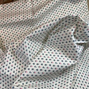 May include: White fabric with a repeating pattern of small pink flowers and dark blue leaves.