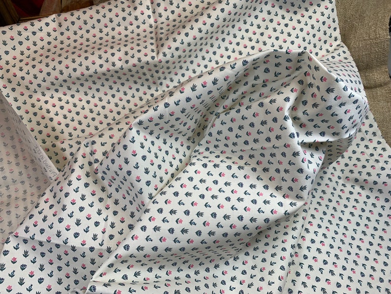 May include: White fabric with a repeating pattern of small pink flowers and dark blue leaves.