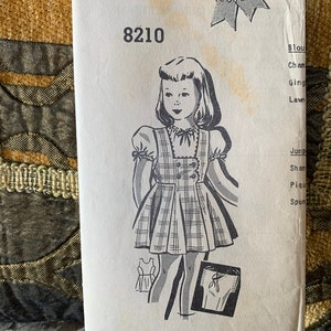 May include: Vintage sewing pattern for a girl's dress and blouse. The pattern number is 8210. The pattern includes instructions for making a dress and blouse in a variety of fabrics, including chambray, gingham, lawn, shantung, pique, and spun rayon.