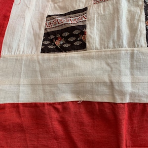 May include: Close-up of a white fabric with red, black, and white patterned fabric sewn together. The fabric has a white seam running across the bottom.