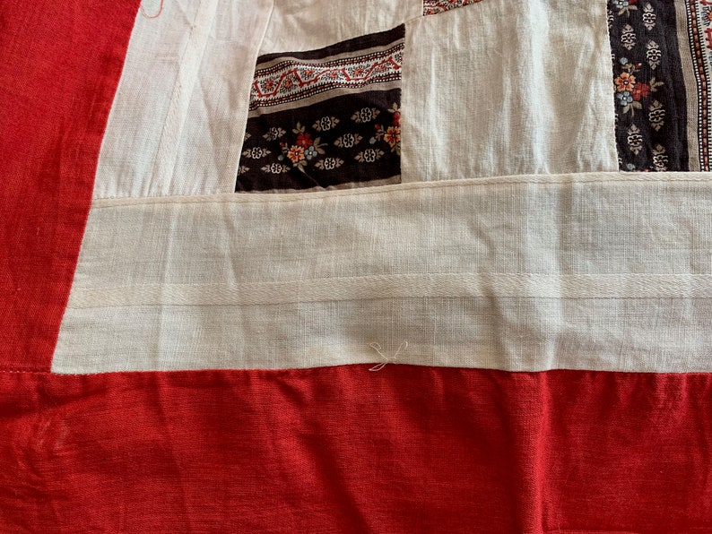 May include: Close-up of a white fabric with red, black, and white patterned fabric sewn together. The fabric has a white seam running across the bottom.