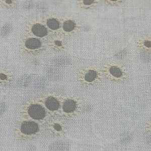Peut inclure: Tissu blanc avec un motif répétitif de petites découpes circulaires. Le tissu a une surface légèrement texturée.