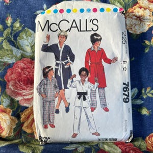Könnte beinhalten: Vintage McCall's Schnittmusterumschlag mit Illustrationen von Kindern in Roben, Pyjamas und einem Karateanzug. Der Umschlag ist weiß mit dem McCall's-Logo und dem Preis $2.25. Die Musternummer ist 7679.