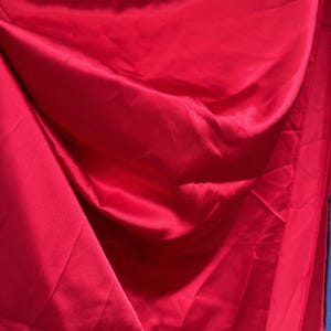 Könnte beinhalten: Nahaufnahme eines glatten, roten Satin-Stoffes mit einem weichen, fließenden Fall.