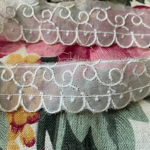 Könnte beinhalten: Weiße Spitzenborte mit einem gewellten Rand und zarten gestickten Wirbeln. Die Spitze ist durchsichtig und hat einen weichen, femininen Look.