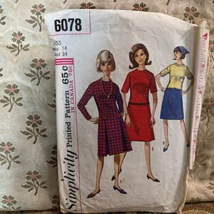 Puede incluir: Patrón de costura Simplicity impreso 65C, un patrón de costura vintage para un vestido. El patrón está impreso en papel blanco con un diseño de vestido a cuadros rojo, negro y blanco. El número del patrón es 6078 y la talla es 14.