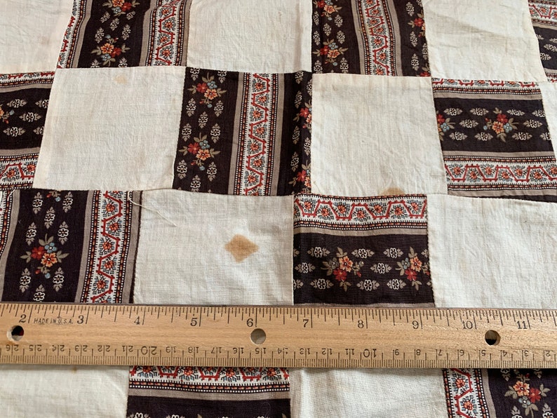 May include: A white quilt with a brown and white floral pattern. The quilt is made of squares and is sewn together with a brown thread. The quilt is measured with a ruler.