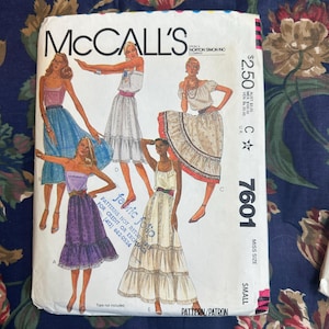 May include: A vintage McCall's sewing pattern envelope featuring illustrations of women's dresses. The envelope is white with the McCall's logo and pattern number 7601. The illustrations depict various dress styles, with the text "fabric folio" and "Tops not included".