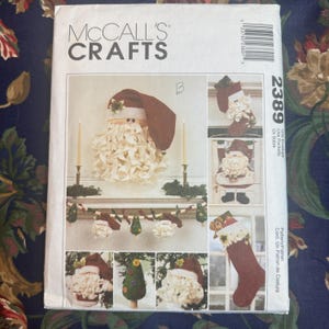 May include: McCall's Crafts pattern featuring Santa Claus-themed decorations. The cover showcases various craft projects, including a Santa Claus head, stockings, and a garland. The pattern includes the number 2389.