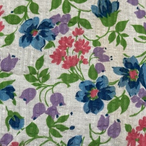 Könnte beinhalten: Ein weißer Stoff mit einem Blumenmuster. Die Blumen sind rosa, blau und lila. Die Blätter sind grün.