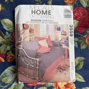 May include: A McCall's Home Decorating pattern envelope. The front features a bedroom scene with a daybed, pillows, and bedding in shades of pink, white, and blue. The text "Bedroom Essentials" is visible.